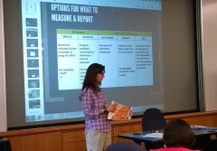 Jennifer Dindinger stands in front of a screen showing a presentation slide titled Options for What to Measure & Report
