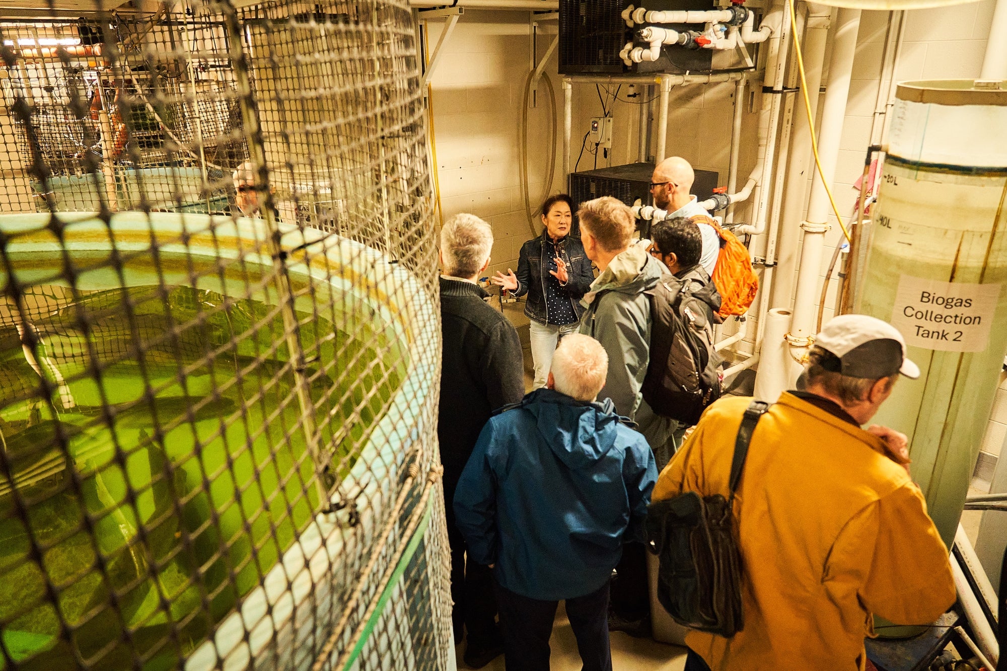 A woman leads six men on a tour of an aquaculture facility with large fish tanks