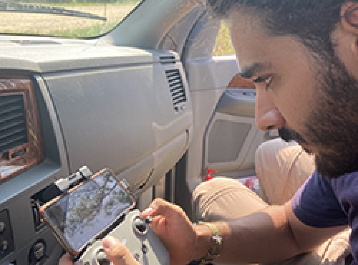 Man with beard sits in car holding equipment used to control drone