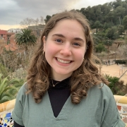 Headshot of Caldonia wearing a black and green shirt in front of trees and a city skyline.