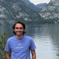 A portrait of Michael Kalinowski standing in front of a large body of water and mountains