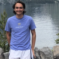 Michael Kalinowski stands in front of a river surrounded by hills.