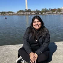 A young woman sits along the water in Washington, DC, with the Washington Monument visible in the distance