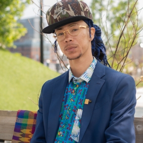 Man sitting on a bench wearing blue jacket, hat, and glasses