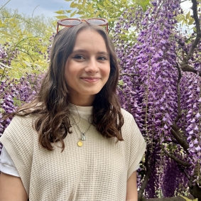 Sabine Malik wearing white shirt in front of purple flowers