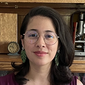 Isabel Butler Viruet, woman with brown hair and glasses in front of a bookcase.