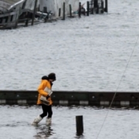 person in a raincoat walking through floodwaters