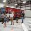 People stand and talk in an aircraft hangar in front of a red University of Maryland Unmanned Aircraft Systems Research and Operations Center trailer