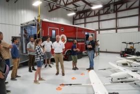 People stand and talk in an aircraft hangar in front of a red University of Maryland Unmanned Aircraft Systems Research and Operations Center trailer